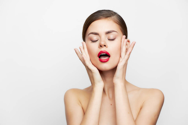 Brunette with bare shoulders Closed eyes keeps hands on face open mouth lipstick - Photo, Image