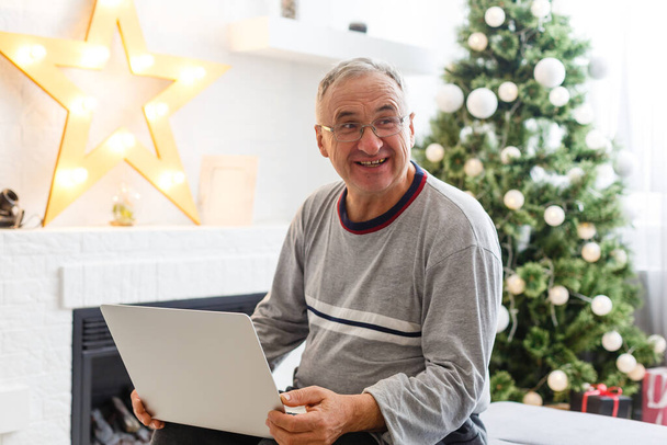 vánoční, svátky a lidé koncept - šťastný usměvavý senior starší muž sedí s notebookem on-line na Vánoce doma - Fotografie, Obrázek