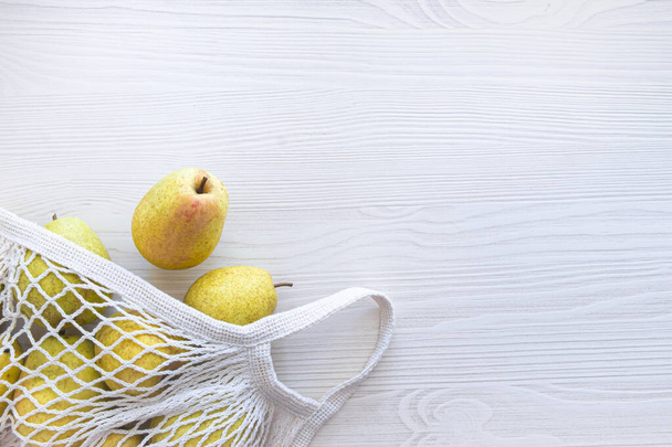 on a wooden light background lies a reusable white knitted eco-friendly bag with fruit pears - Fotoğraf, Görsel