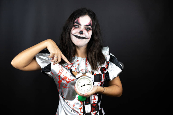 femme dans un costume de clown halloween sur fond noir isolé tenant une horloge - Photo, image