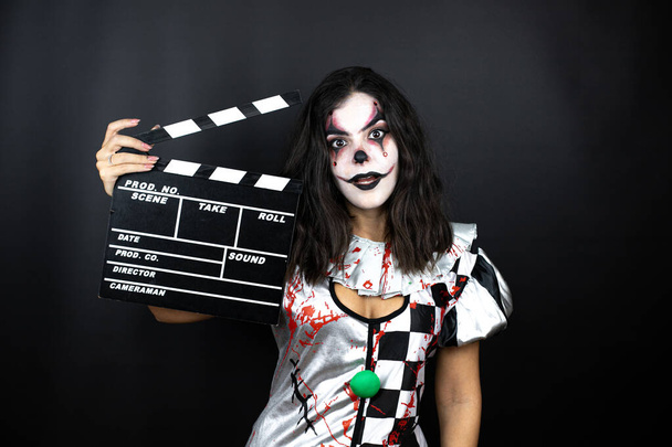 žena v halloween klaun kostým přes izolované černé pozadí držení clapperboard velmi šťastný baví - Fotografie, Obrázek