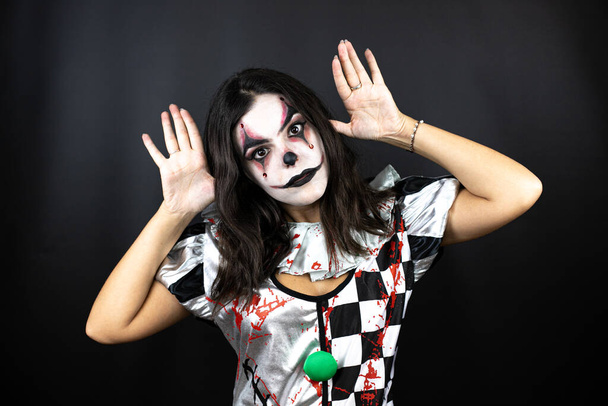 vrouw in een halloween clown kostuum over geïsoleerde zwarte achtergrond doen eng gezicht - Foto, afbeelding