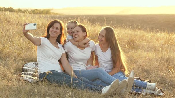 happy family travels, selfie on smartphone in park. mom and healthy children are sitting on a blanket. mother with her daughters is photographed in field on blanket. family travel and adventure - Foto, imagen