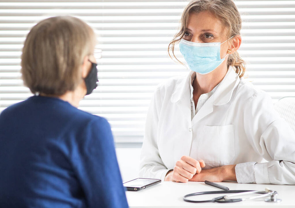 Kadın doktor, tıbbi maske takan bir hastaya danışıyor. - Fotoğraf, Görsel
