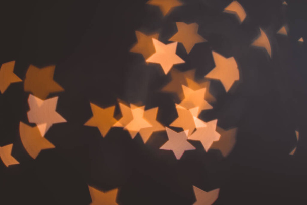 抽象的なボケが黒を背景にクリスマスの星の形を浮かび上がらせます。オレンジと金と黒の色。クリスマスと新年のコンセプト - 写真・画像