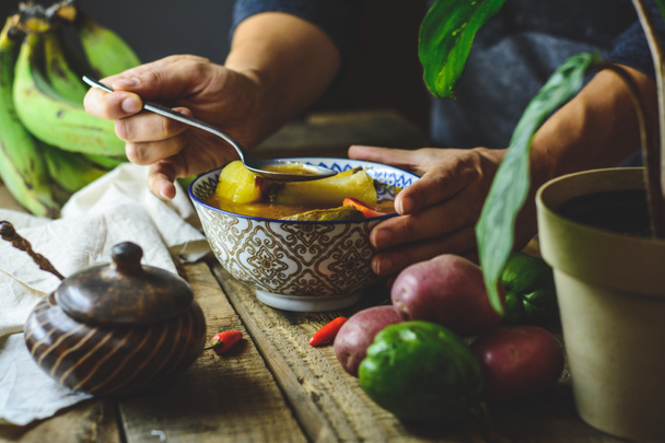 Λαχανόσουπα της Λατινικής Αμερικής, χέρια να πιάνουν το πιάτο. Συστατικά καρότο, τσαγιότ, γλυκοπατάτα, πράσινη μπανάνα πιπέρι. - Φωτογραφία, εικόνα
