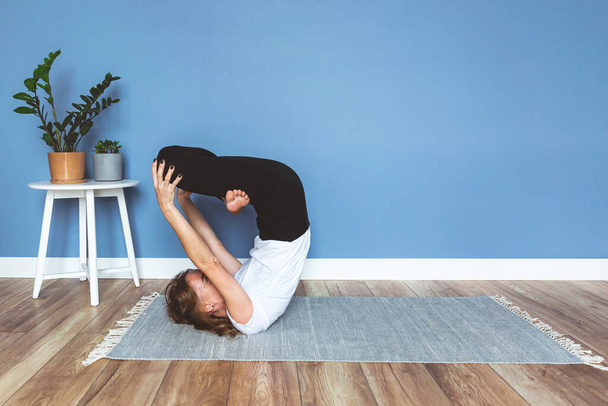 Woman practicing yoga pose at home, blue wall background, copy space. - Фото, зображення