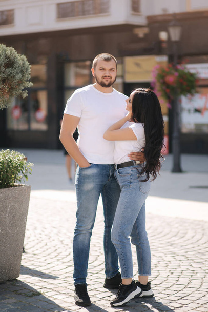 Stylish couple in denim and white t-shirts stand in centre of the city. Late summer concept - Photo, image