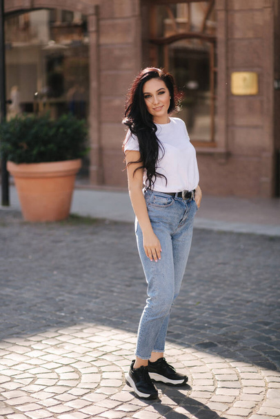 Attraente giovane donna in camicia bianca e jeans che cammina in città - Foto, immagini