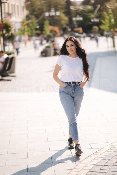 Aantrekkelijke jonge vrouw in wit shirt en jeans wandelen in de stad - Foto, afbeelding