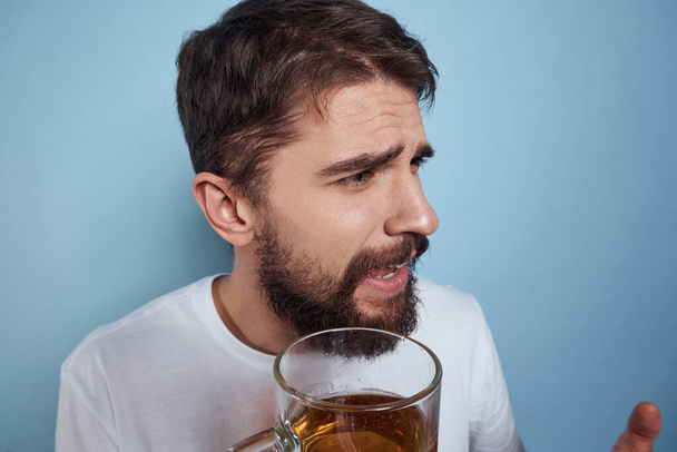 Vidám férfi egy fehér pólóban egy söröskorsóval részeg kék háttér - Fotó, kép