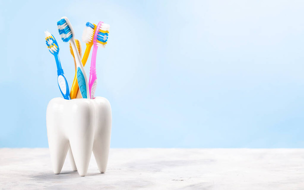 Sok fogkefe egy pohárban egy fog formájában. Kék háttér. A fogkefe kiválasztásának koncepciója - Fotó, kép