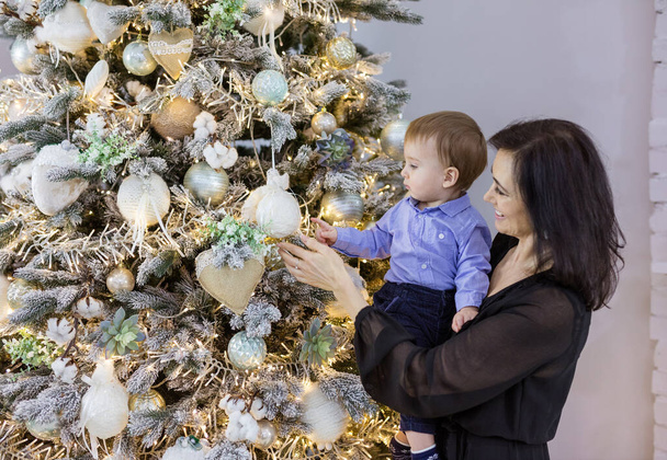 Atractiva mujer madura mostrando adornos en el árbol de Navidad a su nieto bebé en casa - Foto, Imagen