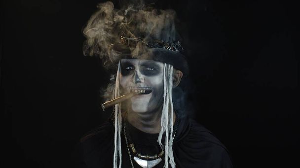 Τρομακτικός άνθρωπος σε σκελετό Απόκριες κοστούμι cosplay καπνίζοντας πούρο, κάνοντας πρόσωπα, χαμογελώντας - Φωτογραφία, εικόνα