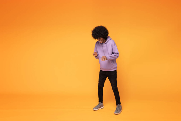 Happy man with afro hair wearing fashionable hoodie , dancing over orange background. - Fotografie, Obrázek