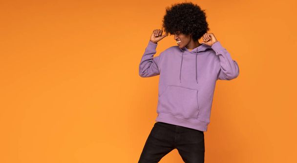 Happy man with afro hair wearing fashionable hoodie , dancing over orange background. - Photo, Image