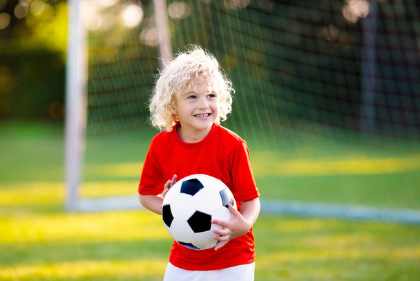Kids play football on outdoor field. Children score a goal at soccer game. Little boy kicking ball. Running child in team jersey and cleats. School football club. Sports training for young player. - Foto, Imagem