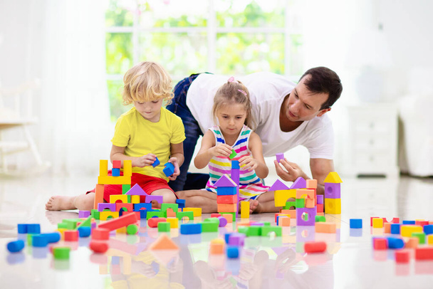 Father and kids play with colorful blocks. Dad, little boy and girl build tower at home or day care. Educational toy for young child. Construction creative game for baby or toddler kid.  - Photo, Image