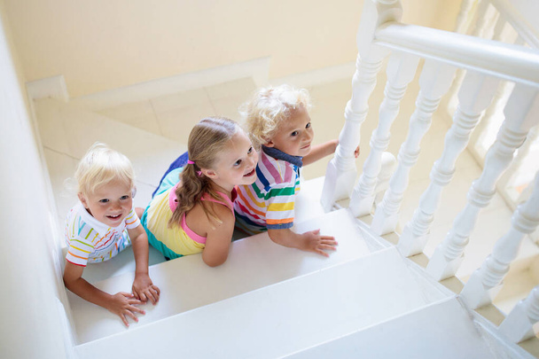 Kids walking stairs in white house. Children playing in sunny staircase. Family moving into new home. Boy and girl on steps of modern stairway. Foyer and living room interior. Child at stair case. - Foto, afbeelding