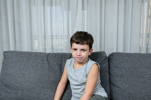 7-jähriges Kind auf der Couch macht ein wütendes Gesicht. - Foto, Bild