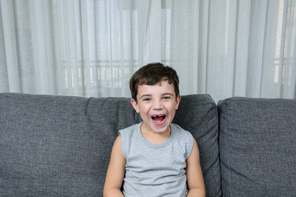 7-jähriges Kind mit zahnlosem Lächeln auf dem Sofa sitzend. - Foto, Bild