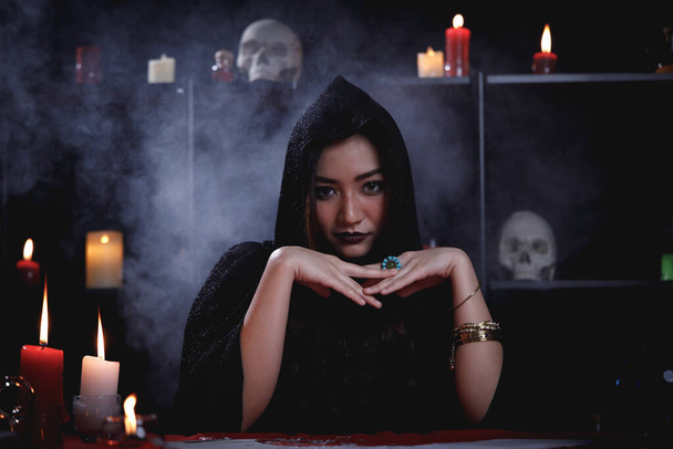 Porträt einer asiatischen Mystery-Wahrsagerin in schwarzem Gewand mit rauchendem Hintergrund. - Foto, Bild