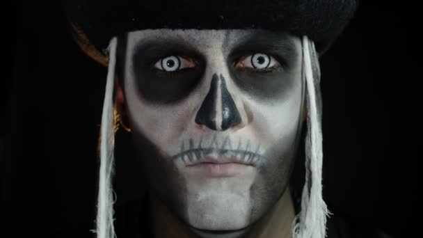 Scary man with carnival makeup of Halloween skeleton opening his eyes against black background - Footage, Video