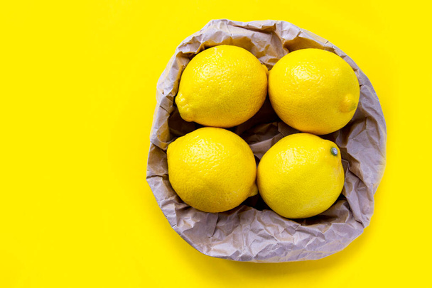 Group of fresh lemon in recycling paper bag. Eco packing concept. Four ripe lemon on yellow background. - Photo, image