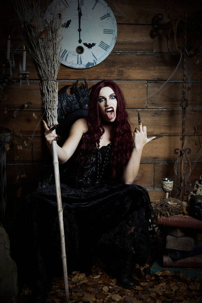Una mujer vestida como una bruja se sienta en un trono gótico en una imagen temática de Haloween - Foto, Imagen
