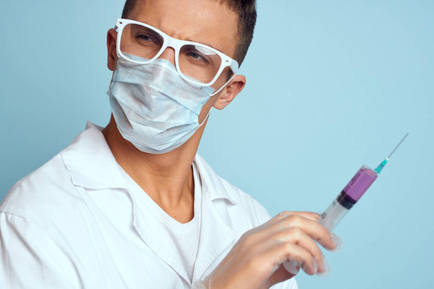 Врач держит шприц в руке с красной жидкостью на синем фоне медицинское платье и защитную маску. - Фото, изображение