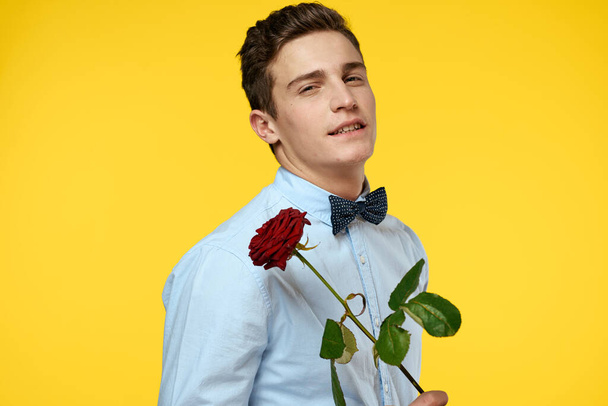 Portrait of a man with a red rose on a yellow background and a light shirt bow tie gentleman - Foto, Imagen