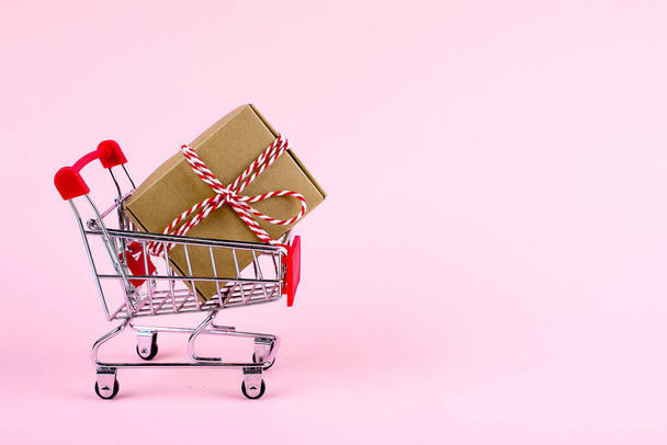Shopping trolley with craft gift present box. Christmas shopping sale, black friday sale concept. Pink background with copy space - Valokuva, kuva