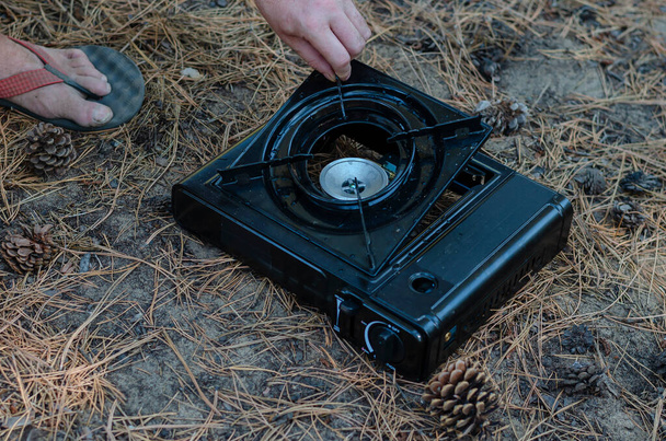 A man collects a portable gas stove in the forest. An adult man's hands set the burner on a black tourist stove. Selective focus. - Photo, Image