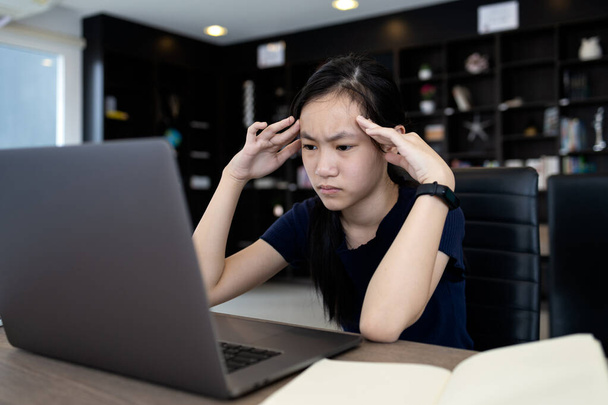 Κουρασμένη ασιάτισσα φοιτήτρια που εργάζεται στο γραφείο, χρησιμοποιεί φορητό υπολογιστή για μεγάλο χρονικό διάστημα στη δουλειά, αγγίζει το κεφάλι με τα χέρια της, κορίτσι που έχει πονοκέφαλο, ζάλη και άγχος, υπερκόπωση ή σύνδρομο όρασης στον υπολογιστή - Φωτογραφία, εικόνα