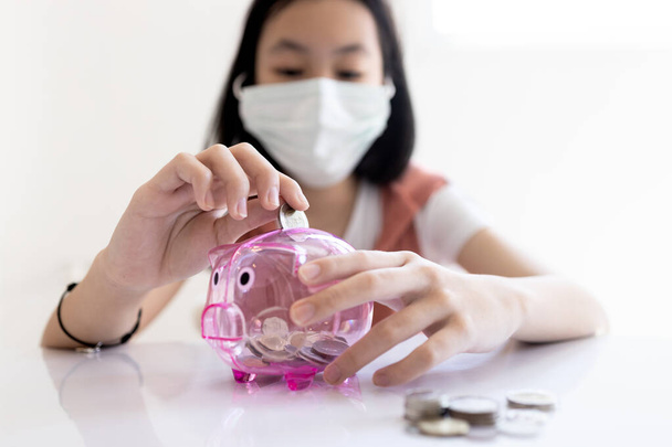 Asijské dítě dívka nosit ochrannou masku, dát mince přes díru v prasátko banky, se snaží ušetřit více peněz na zdravotní péči, pojištění pro Coronavirus, finanční, investice, peníze úsporný plán konkep - Fotografie, Obrázek
