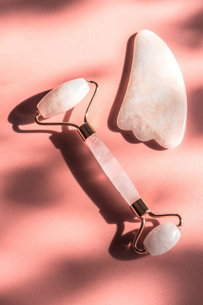 Massage pink natural quartz roller for the face skin care and facial massage with trendy sunny contrasting shadows. Gua Sha tools. Anti age, relaxation lifting at home and alternative medicine concept - Photo, image