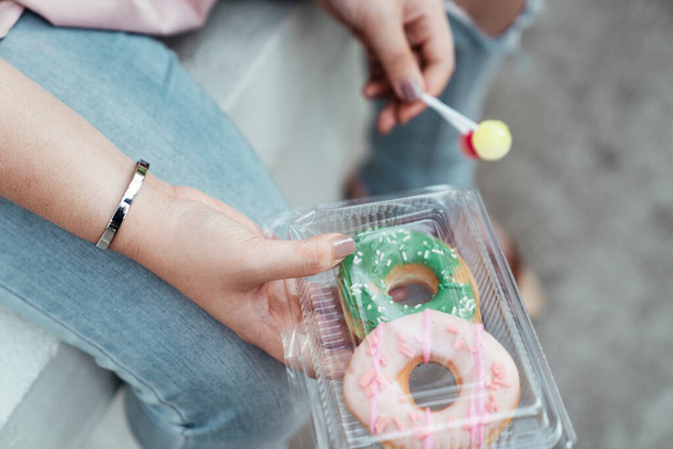 Gehakte afbeelding van snoepjes en donuts in de handen van een dikke vrouw. - Foto, afbeelding