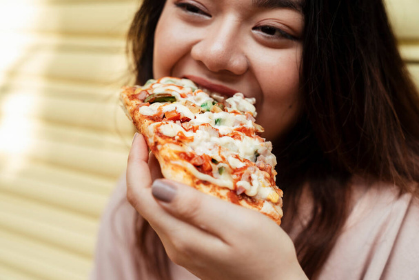 Immagine ritagliata di pizza fatta in casa viene mangiata dalla donna grassa alla porta dell'otturatore giallo. - Foto, immagini