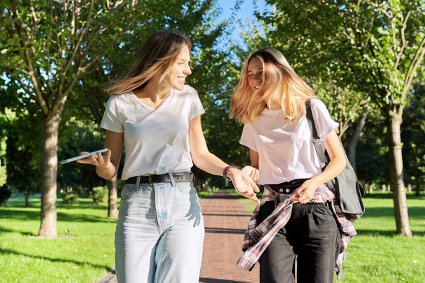 Two beautiful happy girls teenagers 17, 18 years old walking together in park - Фото, зображення