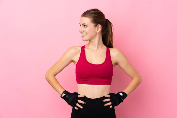 Junge Sportlerin über isoliertem rosa Hintergrund posiert mit Armen an der Hüfte und seitlich blickenden Augen - Foto, Bild