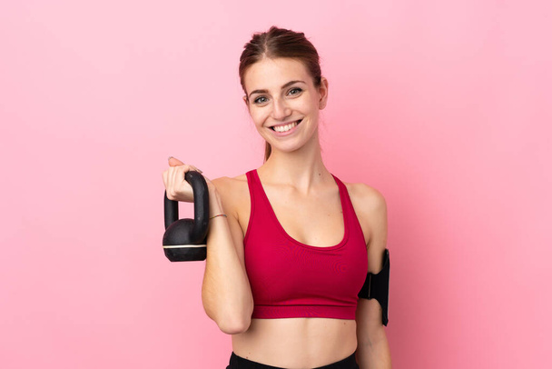 Young sport woman over isolated pink background making weightlifting with kettlebell - Photo, Image