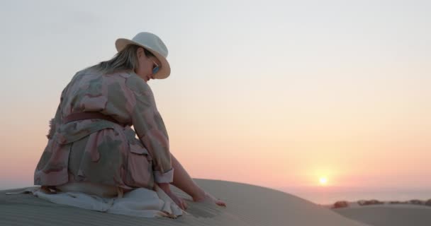 Vrouw overweegt bij gouden zonsondergang en het verdrijven van zand door handpalm - Video
