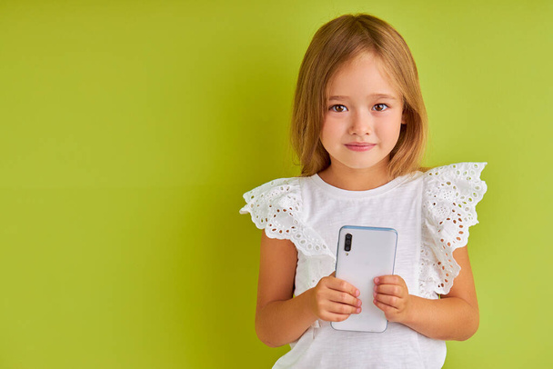 attractive calm little girl hold mobile phone in hands - Foto, afbeelding