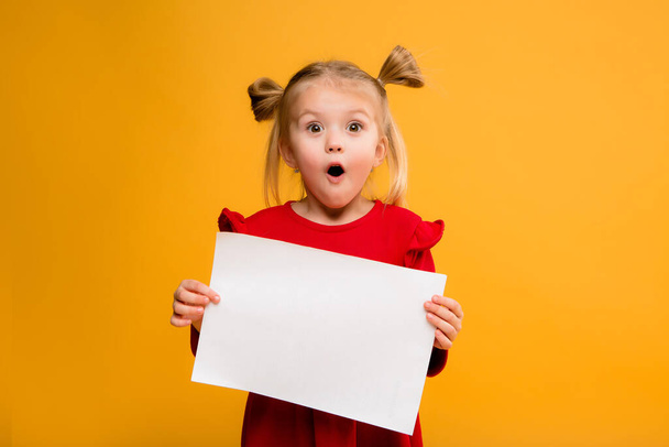 Photo of a girl holding a blank white sheet on a yellow  background. Copy space picture with placement for your text of advertisement - Φωτογραφία, εικόνα