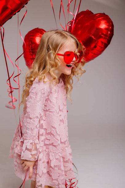 ξανθό κοριτσάκι με ροζ φόρεμα με κόκκινα μπαλόνια  - Φωτογραφία, εικόνα