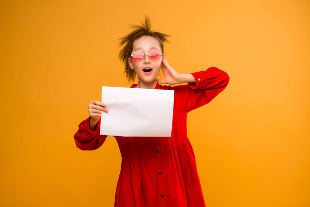 Photo of a girl holding a blank white sheet on a yellow  background. Copy space picture with placement for your text of advertisement - Photo, Image