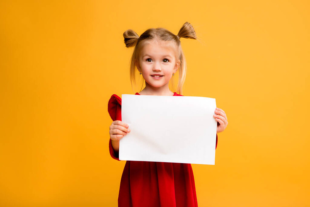 Photo of a girl holding a blank white sheet on a yellow  background. Copy space picture with placement for your text of advertisement - Fotografie, Obrázek