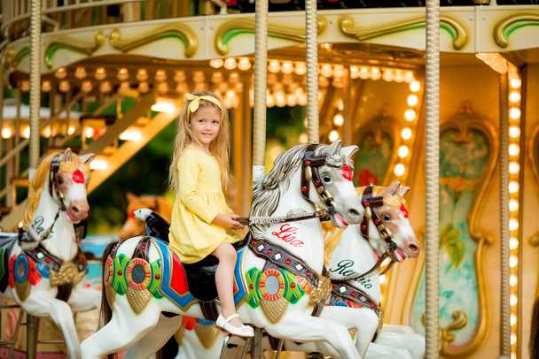boldog szőke kislány sárga ruhában a vidámparkban - Fotó, kép