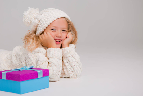 маленька дівчинка в білому светрі з подарунком
 - Фото, зображення
