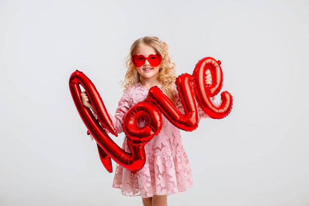 blondynka mała dziewczynka w różowej sukience z czerwonymi balonami  - Zdjęcie, obraz
